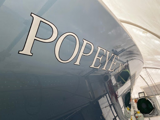 The image showcases a sleek, polished boat with the name "POPEYE" elegantly signwritten on its side. The lettering is in a classic serif font, exuding sophistication and style. The boat appears to be in a well-lit indoor setting, likely a workshop or showroom, where the focus is on quality craftsmanship. The blue paint of the boat enhances the contrast of the white lettering, making it easily readable. This image reflects the expertise of Imagine Signage, a signwriting service that emphasises precision and aesthetic appeal in their work. The meticulous application highlights their attention to detail, making it clear that they cater to clients looking for high-end signwriting services for various applications, including boats, in locations like Brookvale and surrounding areas.