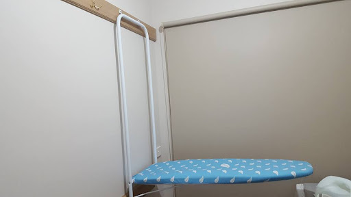 The image depicts a simple, blue ironing board with a white pattern placed against a plain wall. The ironing board is secured by a metal frame that is mounted to the wall, indicating a space-efficient design suitable for smaller areas. The overall setup suggests a focus on home maintenance and tidiness, which could resonate well with clients seeking plumbing services, as it reflects an organised living space.