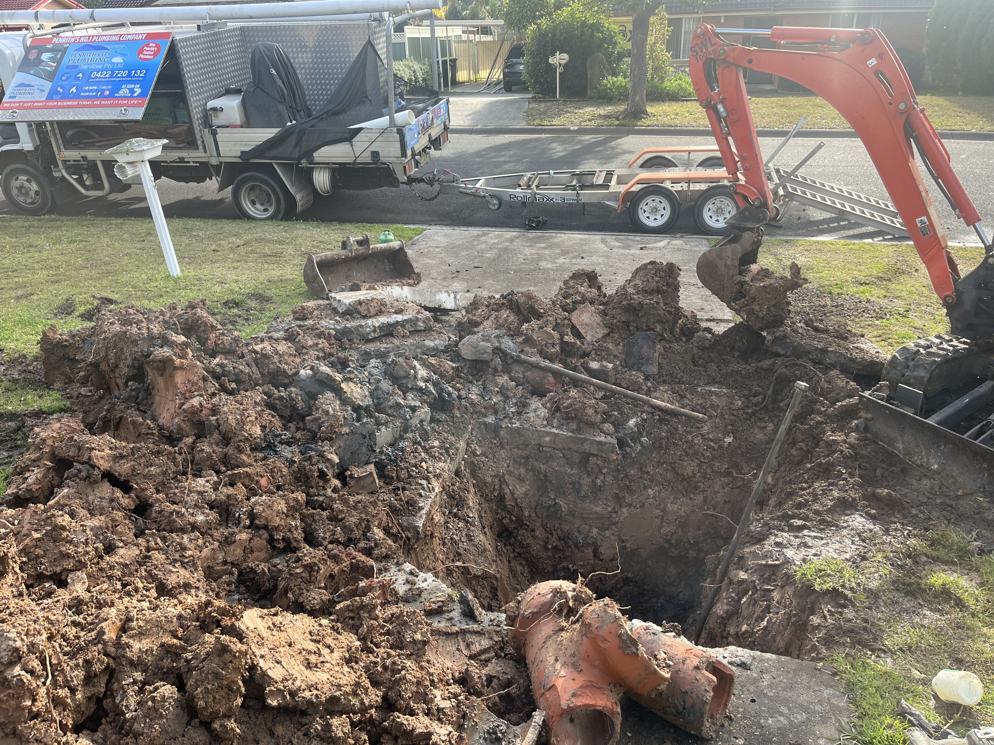 The image depicts a significant excavation site, showcasing a large trench filled with soil and debris. Visible is an excavator actively digging, indicating the ongoing plumbing work. Nearby, a service vehicle can be seen, which likely belongs to the Drain Clearing Penrith business. The scene reflects the challenges and complexity involved in plumbing, especially in drain clearing and repairs. The focus on machinery and trenching suggests that the work is related to underground plumbing systems, crucial for maintaining effective drainage and sewerage management in the area.