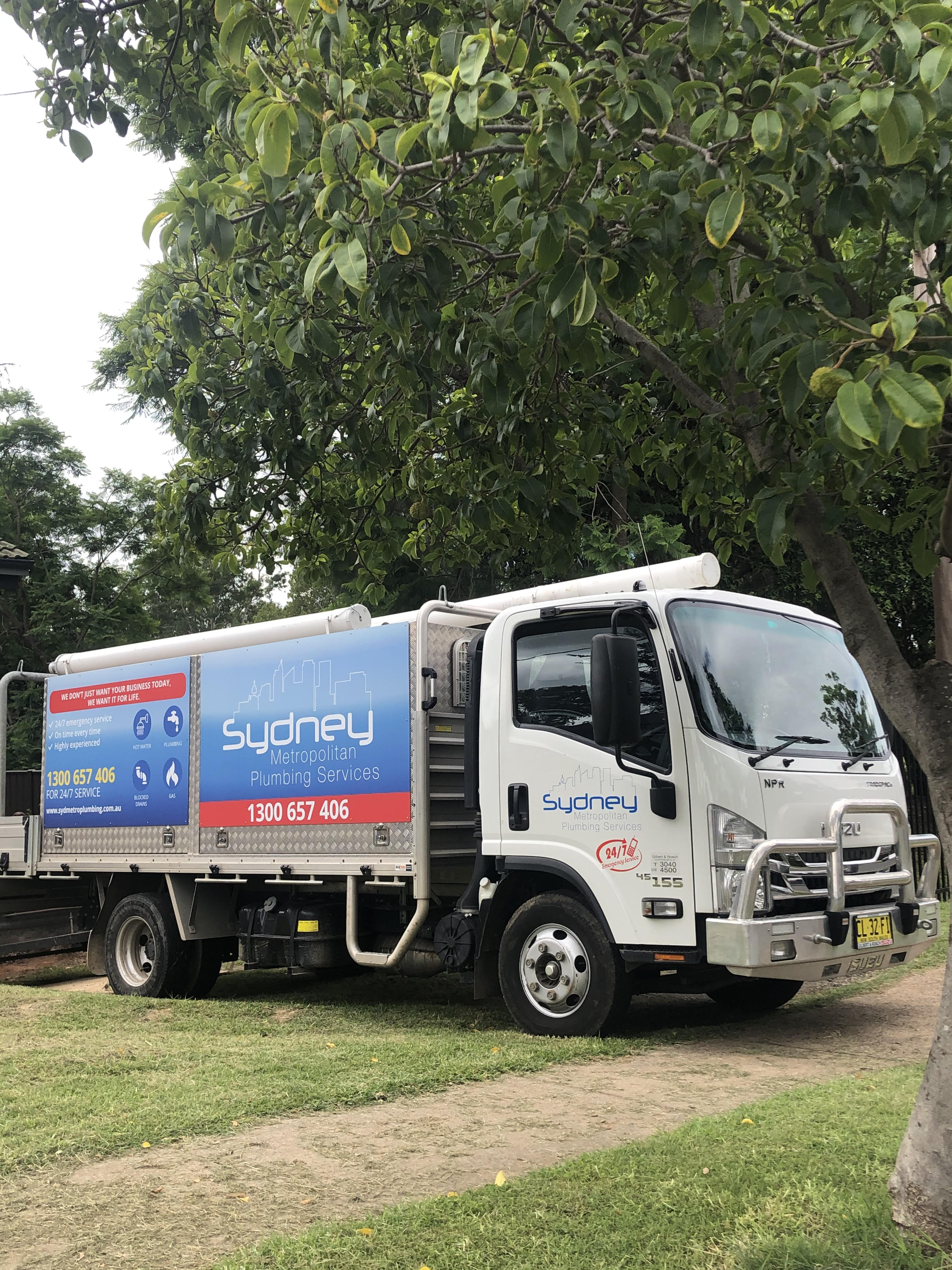 The image features a white service truck, prominently displaying the branding for a plumbing business. It's parked on a grassy area, likely in a residential or commercial neighbourhood in Mulgoa, NSW. The truck has a vivid, colourful design, featuring the name "Sydney Metropolitan Plumbing Services" along with contact information prominently visible. This encapsulates the business’s professional image as it prepares to serve the local community. Surrounding greenery suggests a service-oriented environment, highlighting accessibility and readiness to respond to plumbing needs in the area, including Mulgoa and surrounding suburbs.