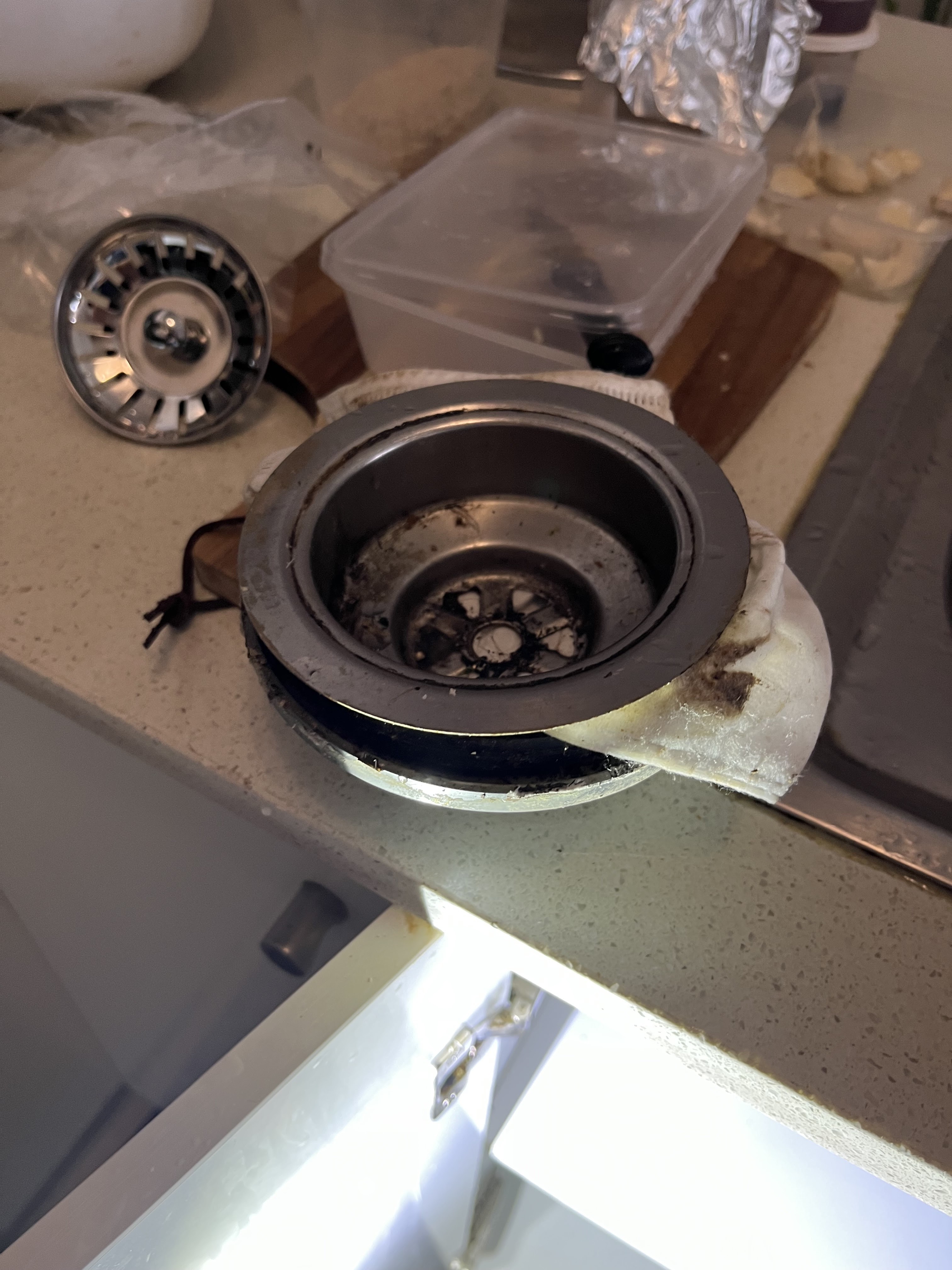 The image depicts a sink waste disposal unit that appears to be disassembled, resting on a kitchen countertop. The unit consists of various components, including the outer casing, grinding chamber, and attachment hardware. Nearby, there are kitchen utensils and a plastic container, indicating an ongoing plumbing repair or maintenance task in a residential kitchen. This scenario is typical for Penrith City Plumbing Services, as they offer expert assistance in resolving issues related to sink disposals and related plumbing problems in Mulgoa and surrounding areas. In such situations, their technicians can provide prompt service to diagnose faults, repair or replace components, ensuring the kitchen is functional and hygienic.