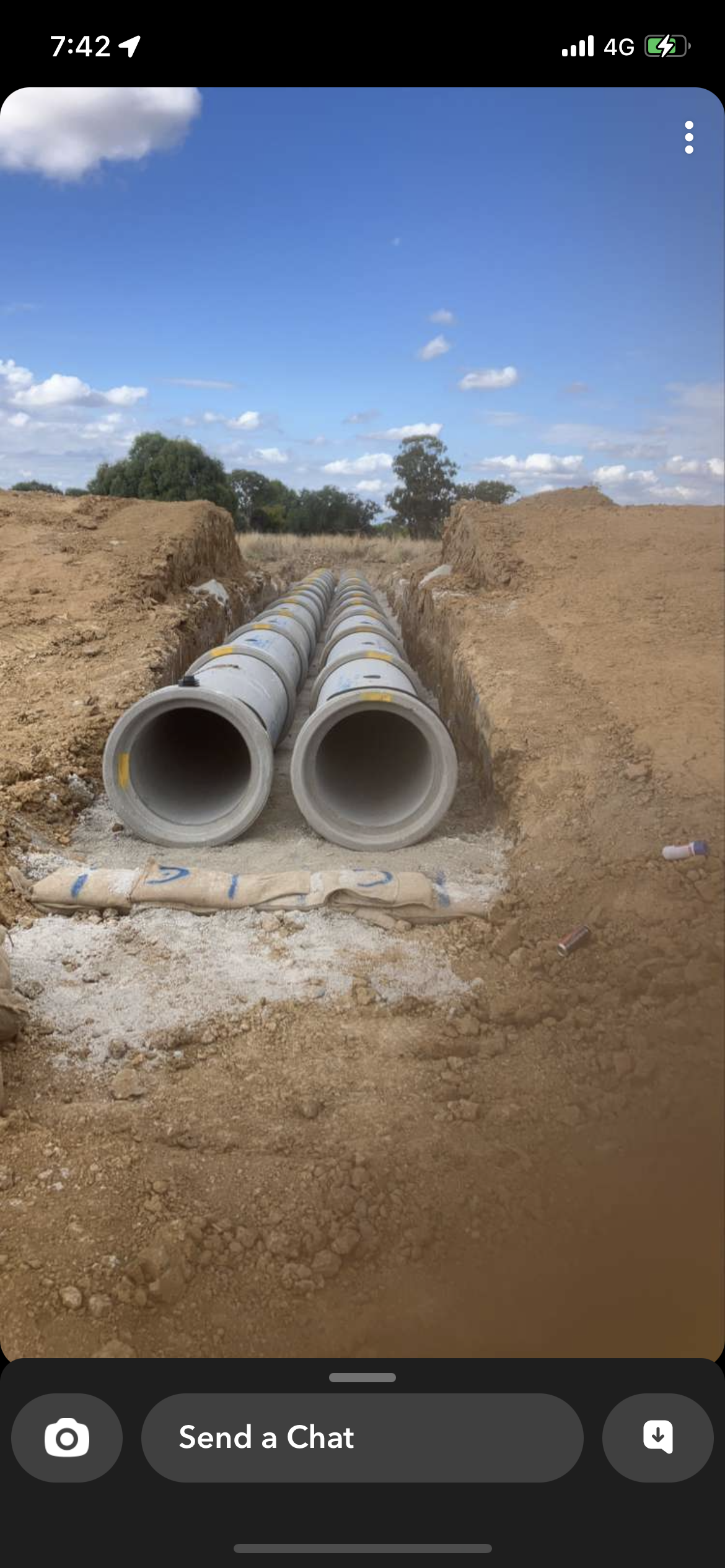 The image depicts an open trench at a construction site with several large concrete pipes laid out neatly. The pipes are positioned in a row along the base of the trench, which appears to have been freshly excavated and is surrounded by mounds of earth. The sky is clear with a few clouds, suggesting good weather for ongoing construction activities. This setup indicates preparation for sewage or drainage installation, commonly required services in plumbing. As Penrith City Plumbing Services operates in Mulgoa, NSW, this type of work aligns with their capabilities. The trenching and installation of large pipes signify a crucial stage in a project that potentially benefits local residential or commercial plumbing systems, ensuring effective drainage and proper waste management.