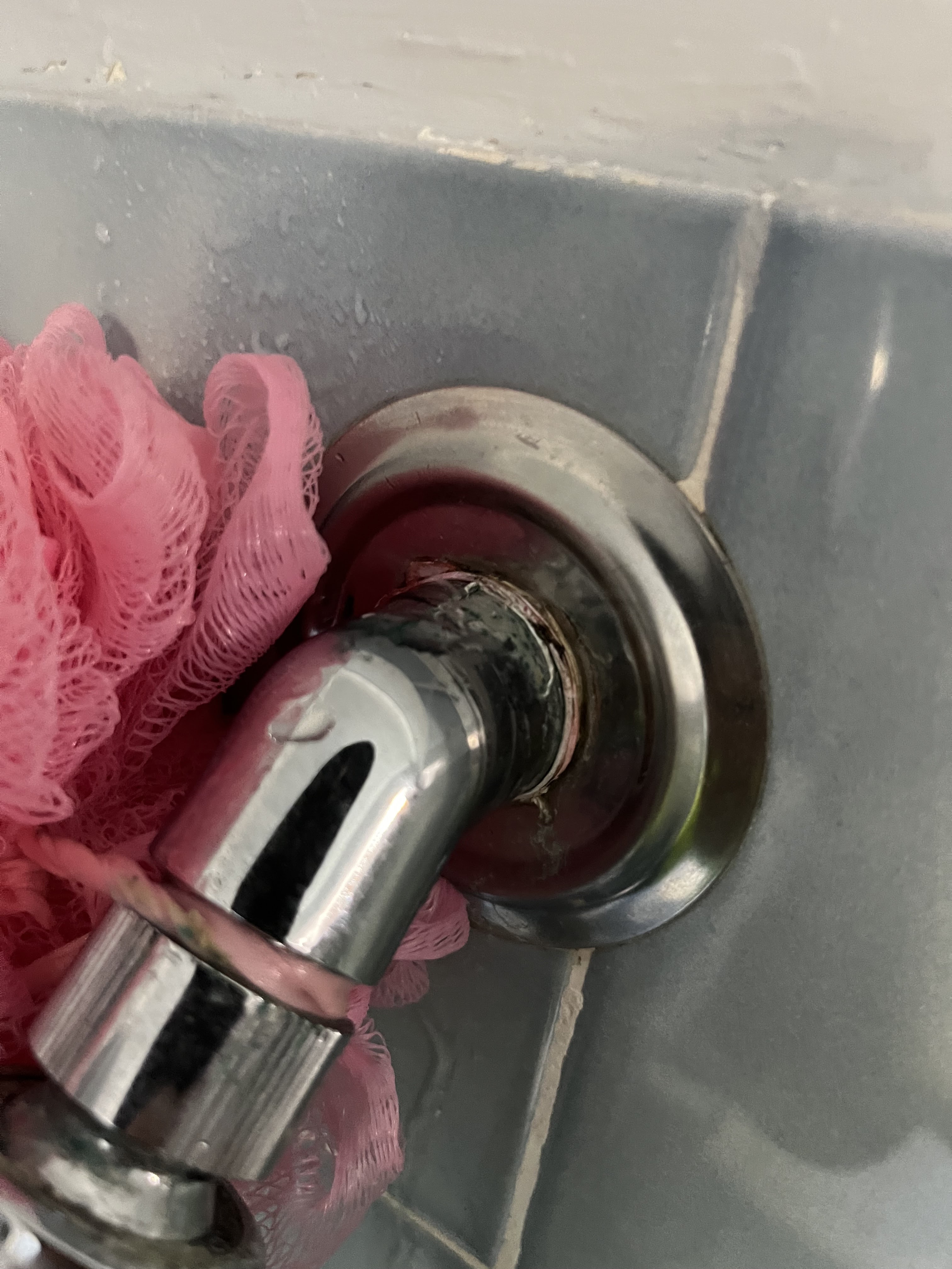 The image portrays a close-up of a plumbing fixture, specifically a chrome-finished tap connected to a wall outlet with a pink loofah hanging nearby. The tap exhibits signs of corrosion around the base, indicating potential water damage or wear over time. The surrounding tiles are grey and show slight water stains, suggesting leakage or inadequate sealing. This situation could be relevant for Penrith City Plumbing Services, as plumbing installations and repairs, particularly in bathrooms, are essential for maintaining proper hygiene and functionality. The company could provide services to address the corrosion, check for leaks, and ensure that the plumbing system is in optimal condition to prevent further damage.