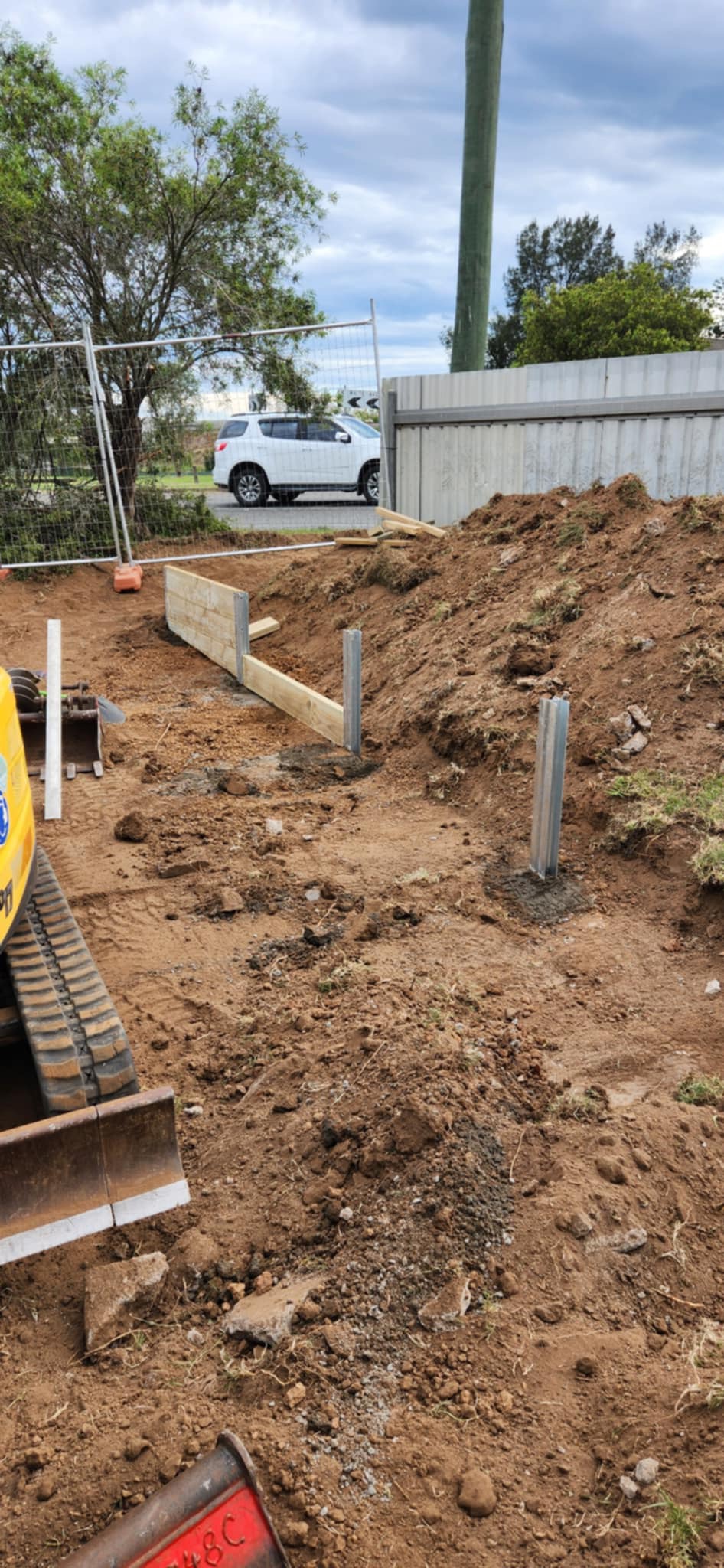 The image depicts an excavation site that’s currently undergoing preparation, likely for plumbing installation or infrastructure development. In the foreground, there are visible wooden forms that outline a foundation, suggesting that concrete may be poured soon. Two vertical metal posts are installed in the ground, which could be for supporting structures or aligning plumbing systems. The surrounding area is bare earth, indicating that landscaping has been cleared to accommodate plumbing work or construction. The presence of machinery tracks in the lower part of the image implies excavation equipment has been used on-site, which is common in plumbing projects when laying underground pipelines or sewage systems. The overall scene indicates a bustling work zone, reflecting the active and professional nature of Penrith City Plumbing Services in carrying out necessary plumbing projects.