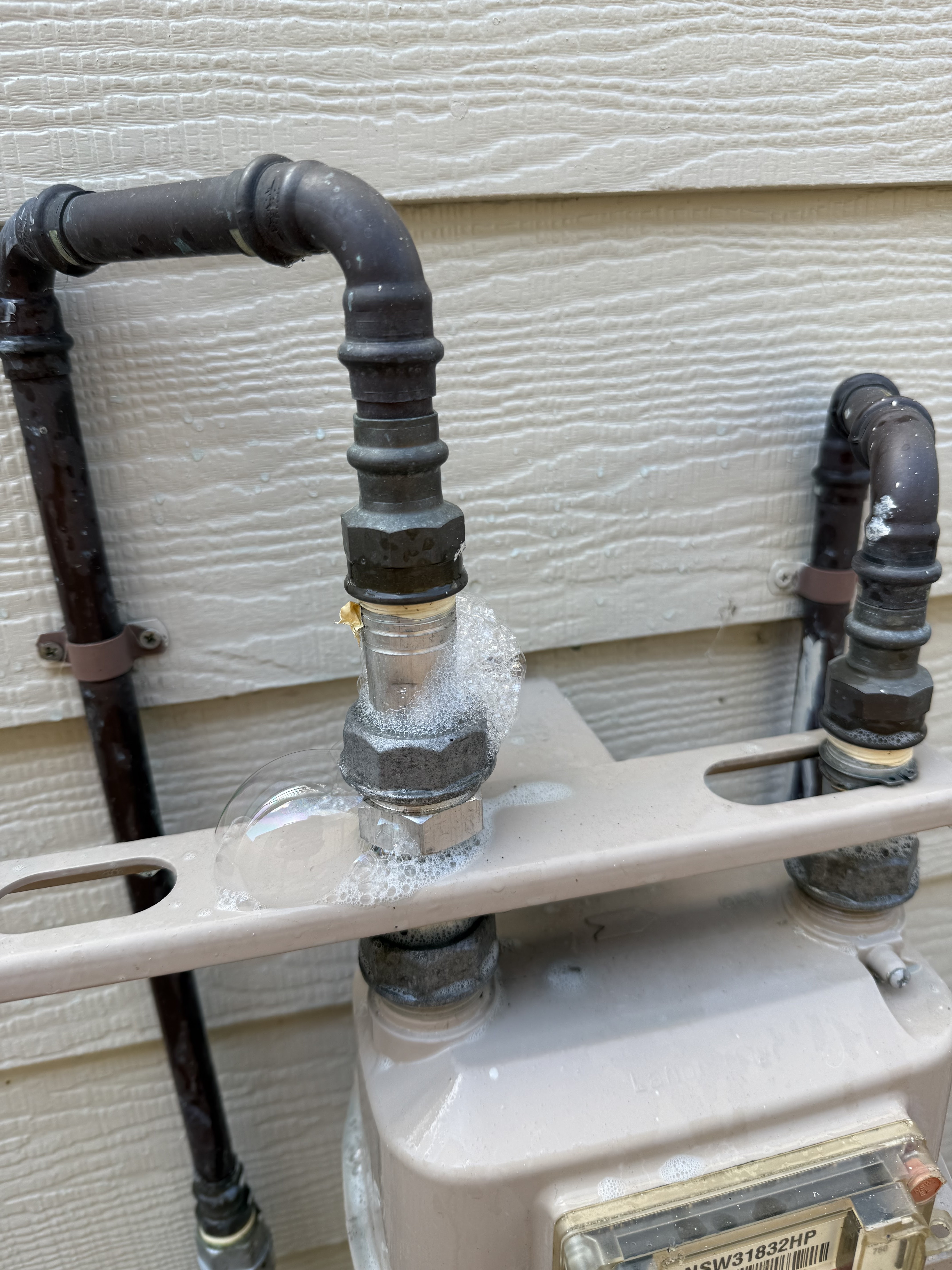 The image shows a gas meter with several pipes connected to it, where one of the fittings appears to be leaking, as indicated by the presence of bubbles forming around the joint. This situation is critical as it suggests a potential gas leak, which can be dangerous. In the context of Penrith City Plumbing Services, a plumber would need to address this issue promptly to ensure safety and compliance with relevant regulations. The plumber would likely need to inspect the connection, possibly replacing the faulty fitting to stop the leak and ensure that the gas system operates securely.