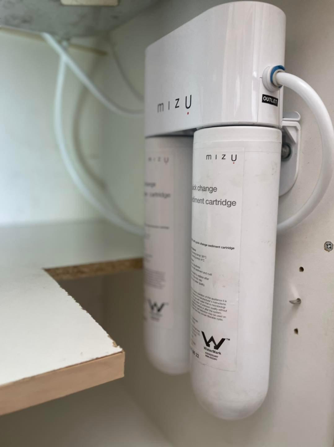 The image displays a water filtration system installed under a kitchen sink. The system consists of two sediment cartridges and is branded 'mizu'. These cartridges are designed to improve water quality by removing sediments and impurities, ensuring safe and clean drinking water for the household. The plumbing setup appears tidy, with clear connections and labelled outlets, indicating proper installation. This setup aligns with the services offered by Penrith City Plumbing Services, highlighting their expertise in residential plumbing and water filtration systems.