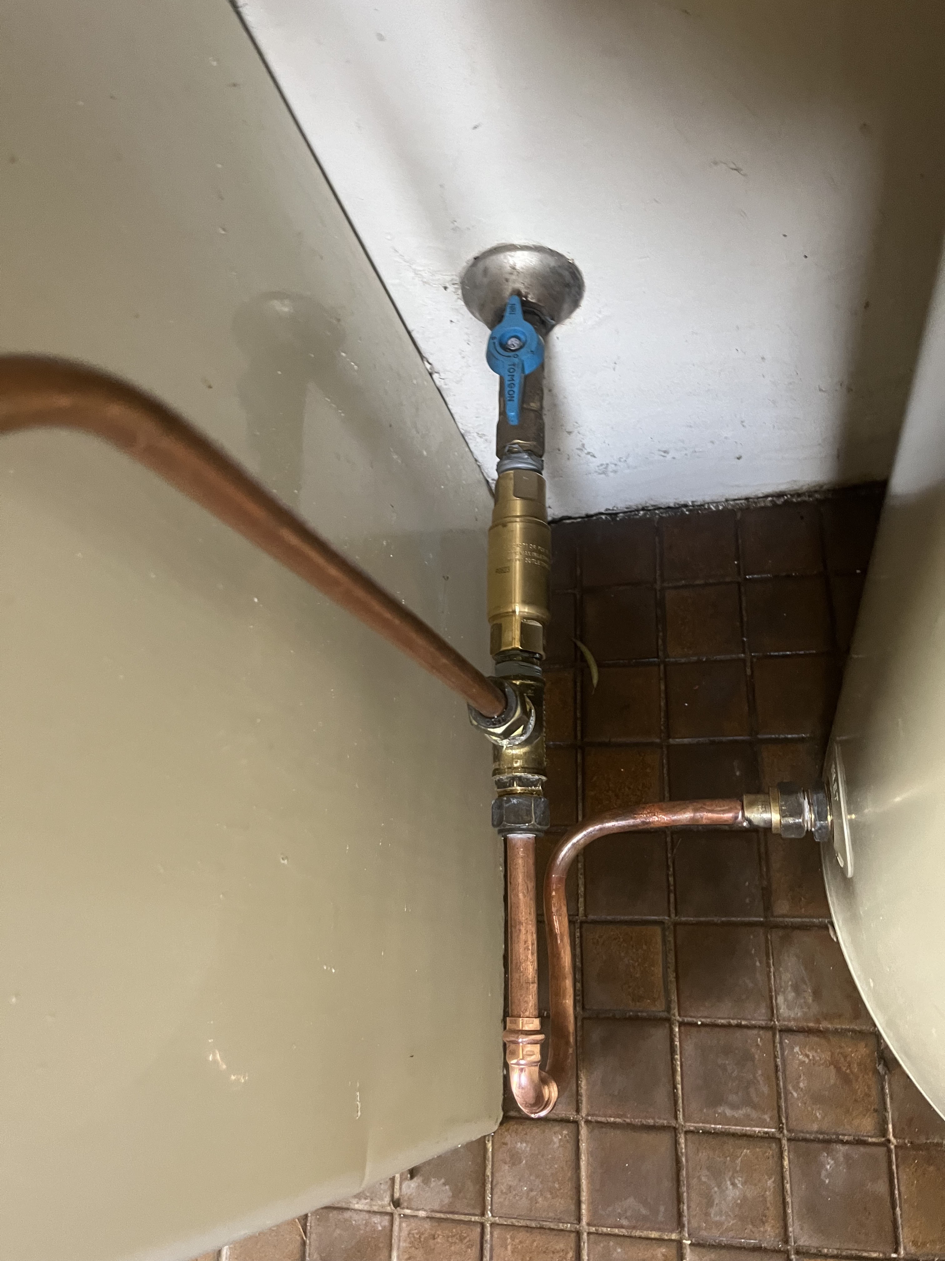 The image features a copper plumbing installation with a valve and piping connected to a water heater. The valve is blue and is situated near the wall. The surrounding floor is tiled.