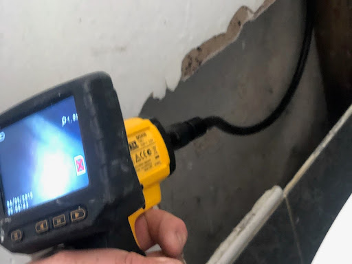 The image depicts a plumber using a handheld inspection camera, commonly referred to as a borescope, to inspect a hidden area behind a wall. The camera is aimed at a section of the wall where the surface is peeling, possibly indicating a leak or water damage. This tool allows the plumber to get a clear view of the internal structure without the need for intrusive demolition. The context suggests that Penrith City Plumbing Services is utilising advanced technology to diagnose plumbing issues efficiently for their clients in Mulgoa and surrounding areas, demonstrating their commitment to quality service and thorough inspections.