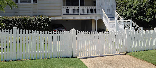 The image depicts a charming residential property featuring a white picket fence that outlines the front garden. The fence is well-maintained, with pointed tops giving it a classic appeal. There is a neat pathway leading up to the house, bordered by lush green lawn and shrubs, indicating a well-kept landscape. A car is visible parked in the driveway beneath the house, which adds to the homely atmosphere. This setting not only highlights the aesthetic purpose of quality fencing but also its practical role in defining property boundaries and enhancing security. As a fencing contractor, Miller's Fencing and Retaining Walls can draw attention to their installation of robust, stylish fences like the one shown, which contribute to the overall curb appeal of a home while providing essential functionality.