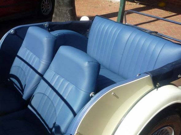 The image showcases a pair of elegantly upholstered seats in a classic vehicle, featuring a rich, blue leather finish. The seats are designed with vertical stitching and a streamlined shape, emphasising a vintage aesthetic. The two-seat configuration suggests a convertible or an open-top vehicle, highlighting the attention to detail and craftsmanship typical of vehicle restoration services. The interior appears clean and well-maintained, signalling the high standards upheld by Horgans Auto Upholstery in their restoration projects.