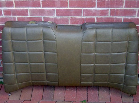 The image shows a brown, faux leather bench seat, reminiscent of classic car upholstery. The seat features a quilted pattern, with a central section that lacks back support, likely designed for a vehicle's rear. The clean lines and vintage style suggest it may be a component for a classic car restoration. The unique shape and colour could indicate its use in a muscle or vintage car, appealing to car enthusiasts looking to restore their vehicles to original specs.