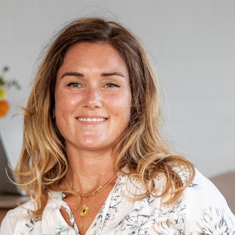 The image features a woman with long, wavy hair and a friendly smile, dressed in a floral top. The background is softly blurred, suggesting a calm and welcoming environment, which aligns with the soothing and holistic nature of naturopathy. The woman's expression conveys warmth and approachability, ideal for a health-focused business like Herb Bar, promoting a relaxing and supportive atmosphere for clients seeking naturopathic services.