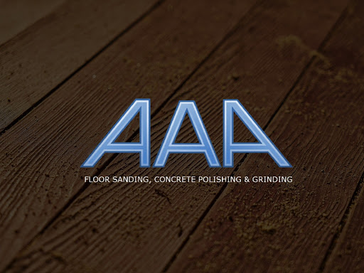 The image prominently features the logo of AAA Floor Sanding, Concrete Polishing & Grinding, displayed against a background that resembles wooden flooring. The background highlights the texture of wooden planks, which is fitting for a flooring specialist. The logo is designed with a modern and sleek font, and the letters 'AAA' are emphasised in a light blue hue, making them stand out against the darker, earthy tones of the background. The tagline below clearly indicates the services offered by the business, reinforcing their expertise in flooring solutions.
