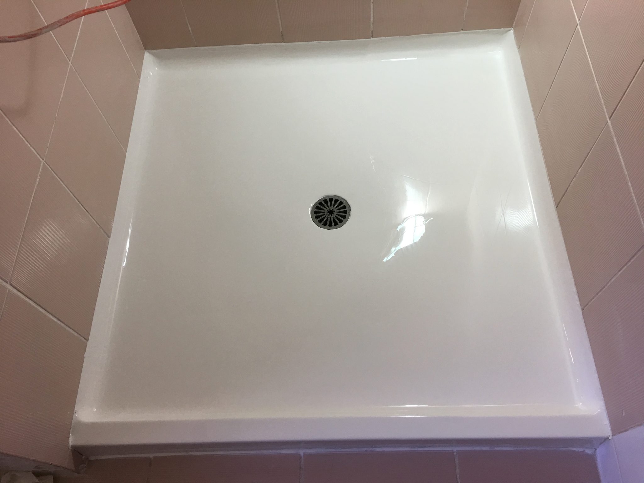 The image shows a freshly installed shower base, likely part of a bathroom renovation project by Coastline Bath Resurfacing. The shower base is white, sleek, and shiny, indicating a high-quality resurfacing job. The drain in the centre is modern and well-aligned, indicating that the installation has been done with precision. The surrounding tiles appear to be pink, suggesting a cohesive aesthetic choice that may complement the rest of the bathroom. This installation reflects the company's commitment to enhancing bathroom spaces in Kyogle and surrounding areas, ensuring that each element is both functional and visually appealing. This shower base is ready for use, indicating that the renovation process is either complete or nearing completion.