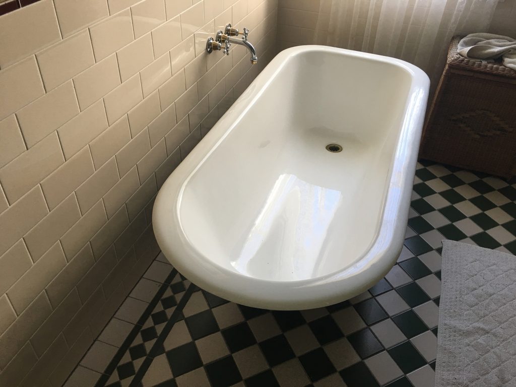 The image showcases a sleek, white bathtub positioned in a bright bathroom setting. The bathtub's smooth curves and glossy finish indicate it is well-maintained, highlighting the quality of materials often used in bathroom renovations. The tiled floor features a classic pattern, adding a touch of elegance to the overall ambience. Natural light filters through a window, enhancing the inviting feel of the space. This setting is ideal for Coastline Bath Resurfacing, as it may inspire potential clients looking to update or remodel their bathrooms. The clear condition of the tub suggests a recent resurfacing, an essential service offered by the company to refresh and rejuvenate bathrooms in the Kyogle area and its surrounding locations.