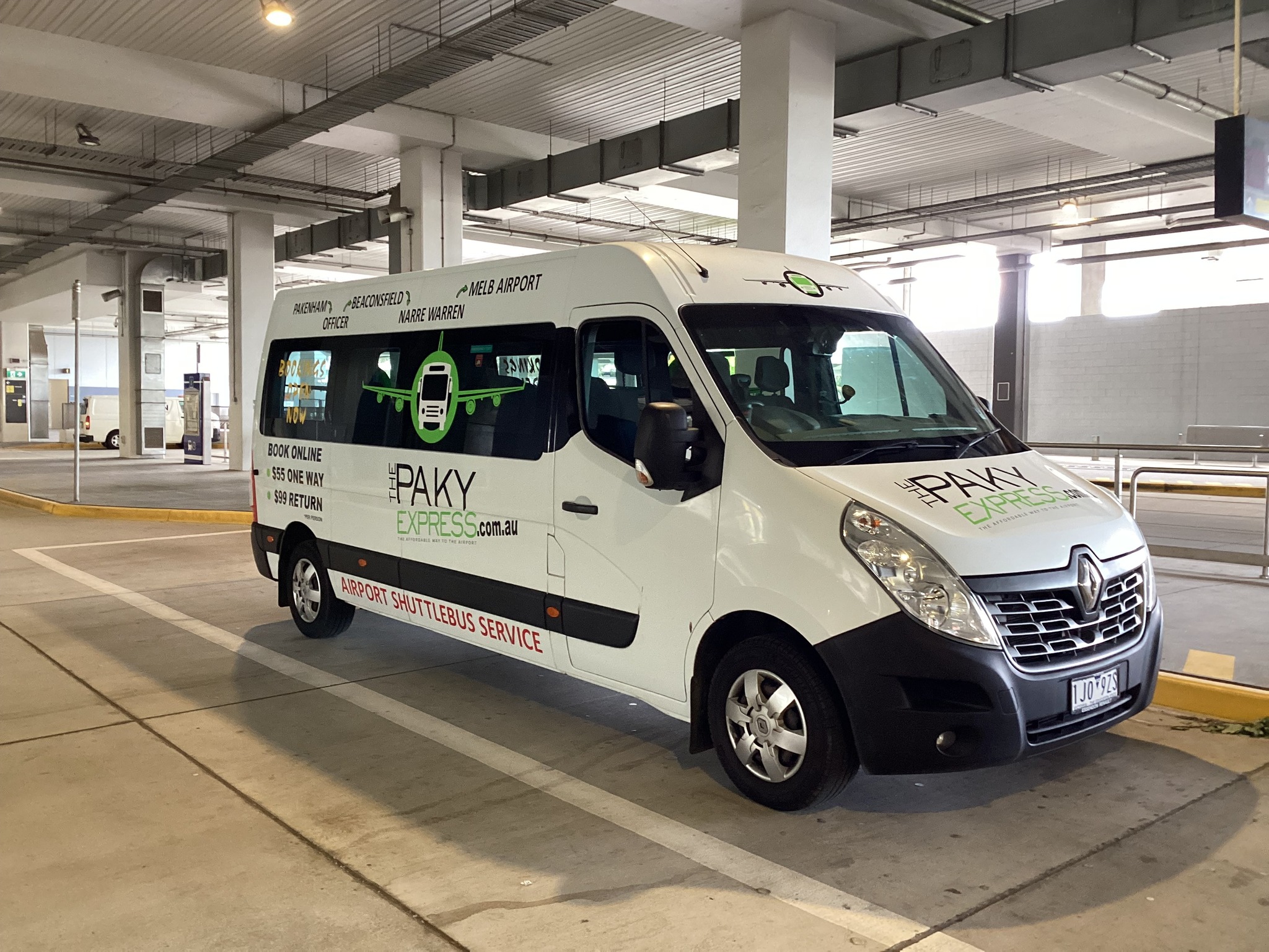 The image features a white van belonging to Paky Express, an airport shuttle service based in Hallam, VIC 3803. The van is parked in a spacious area, likely within an airport parking structure, indicated by the concrete surroundings and overhead lighting. The vehicle is branded with the Paky Express logo prominently displayed on its side, along with the website and service information. This suggests that the van serves as both a transport vehicle and a mobile advertisement for the business. No passengers are visible in the image, highlighting the van as ready for service. Given the context, this vehicle is likely awaiting passengers for airport transfers from various serviced locations such as Eumemmerring, Endeavour Hills, and Narre Warren, contributing to the convenience and efficiency of airport travel for customers in the area.