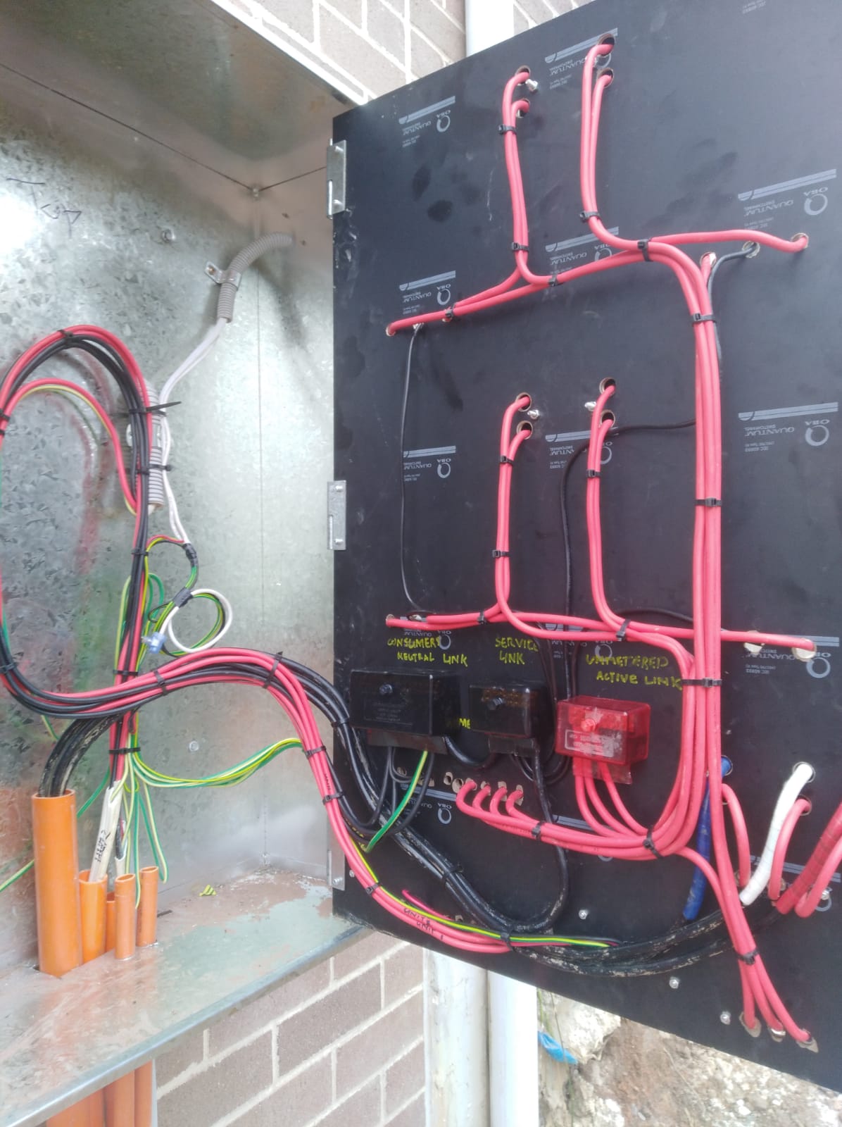 The image depicts an electrical distribution board with various wires organised and labelled. There are clearly marked connections for "unpowered neutral link", "serviced link", and "unpowered active link". The use of different coloured wires, particularly red and black, indicates various circuits and safety components. The panel is well-arranged, reflecting professionalism and attention to detail, which is crucial for ensuring safety and efficiency in electrical services. This setup is typical for an electrician in residential or commercial properties in West Ryde, NSW, ensuring all connections are made safely and according to local regulations.