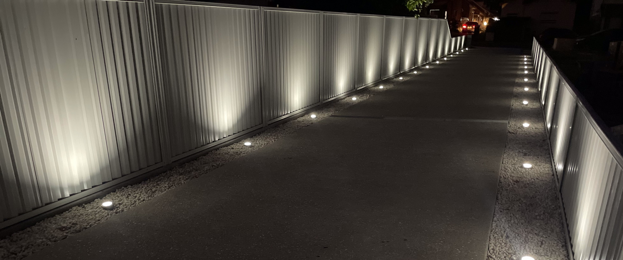 The image showcases a beautifully illuminated pathway, flanked by a sleek, modern fence. The low-level LED lights are strategically placed along the walkway, enhancing safety and aesthetics during the night. This design is ideal for residential properties, providing both illumination and style, making it a perfect feature for homes in West Ryde and surrounding areas.