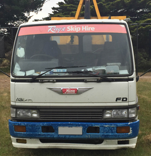 The image shows the front view of a white and blue Hino truck. The windscreen banner displays the name 'Ray's Skip Hire' in red and white text on a red background. This truck appears to be part of the Skip Hire Phillip Island earthmoving business, used for transporting skip bins and earthmoving materials in and around Smiths Beach and nearby locations on Phillip Island, VIC 3922.