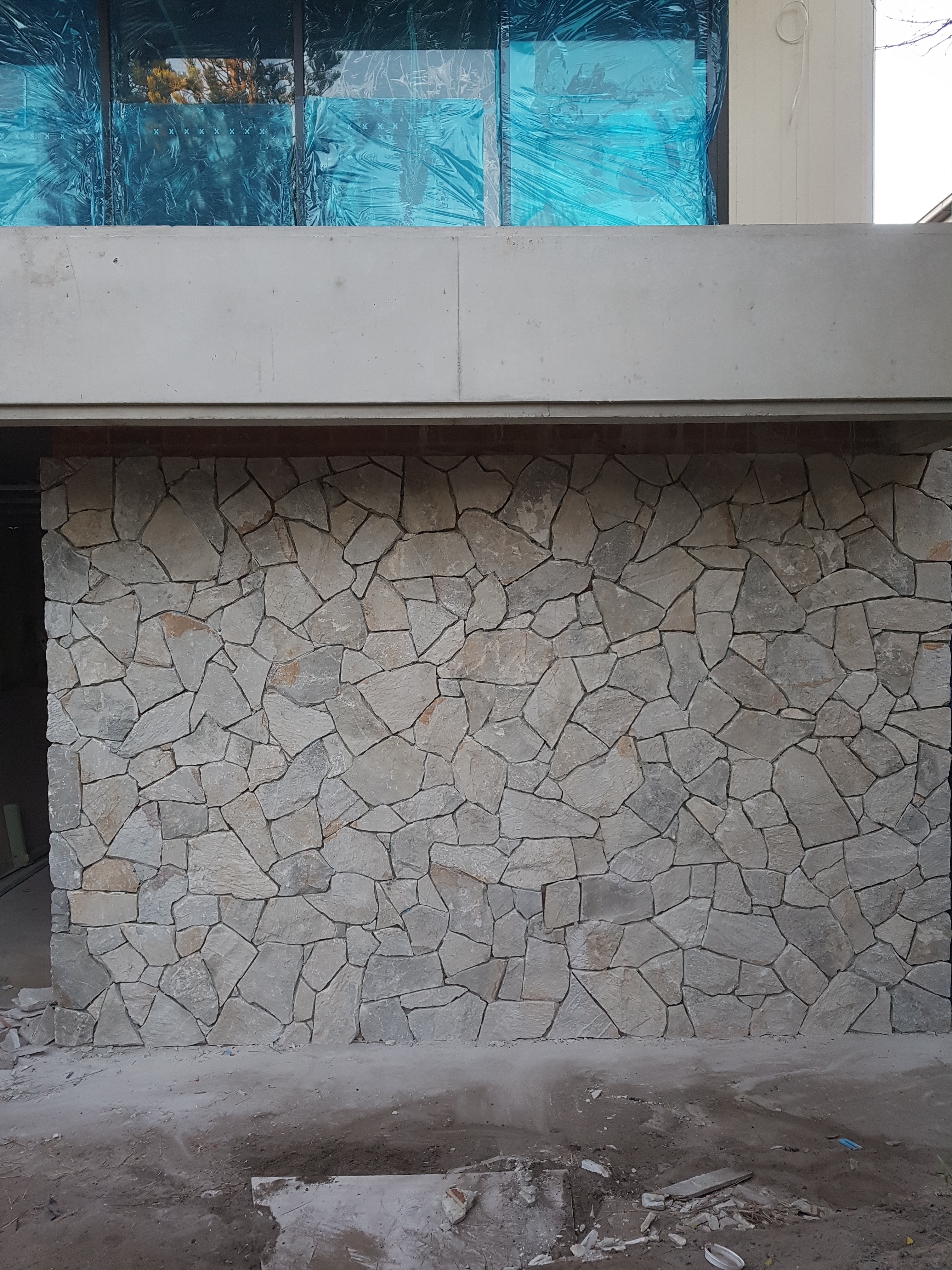 The image showcases a beautifully crafted stone wall, indicative of high-quality stonemasonry work typical of the Masters Bricklaying and Stonemasonry business. The wall features an irregular arrangement of variously-sized stones, which adds texture and visual interest. The stones are set in a sturdy, composite manner, ensuring durability and aesthetic appeal. This construction serves as a decorative element for a building under construction, as suggested by the presence of plastic sheeting in the upper portion of the image, hinting at ongoing renovations or new builds. The environment projects a professional and meticulous approach to bricklaying and stonemasonry, reflecting the company's expertise in servicing the Cremorne area and surrounding locations like Cammeray and Mosman. Overall, the image captures the essence of craftsmanship and attention to detail that clients can expect from Masters Bricklaying and Stonemasonry, positioning them as a reliable choice for stonemasonry projects.